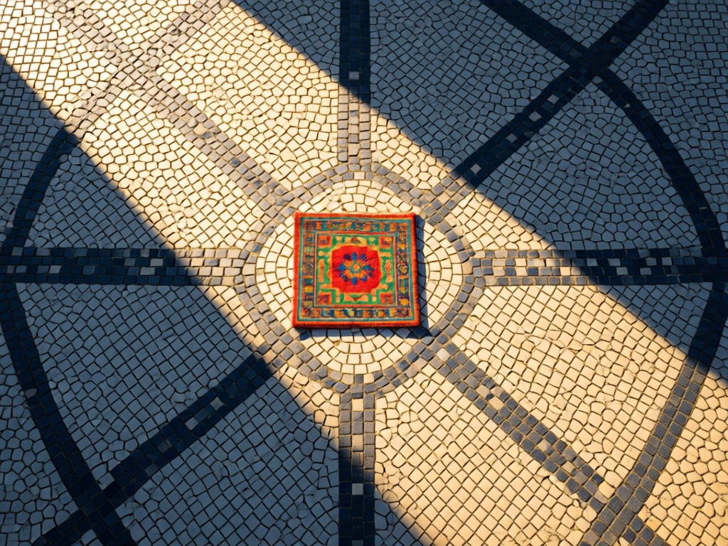 Aerial view of traditional Portuguese calçada pavement pattern with a single vibrant fabric swatch placed at center. Morning light creating geometric shadows. No people.